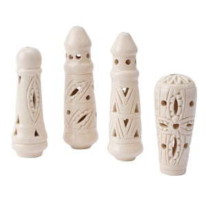 May include: Four off-white, carved candle holders with intricate cut-out designs. The candle holders have varying shapes, including cylindrical and rounded tops, with geometric and floral patterns. They are arranged against a white background.