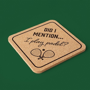 Puede incluir: Posavasos cuadrado de corcho con el texto "DID I MENTION... I play padel?" en negro. El posavasos presenta un contorno negro y un gráfico de dos raquetas de pádel y una pelota. El fondo es verde oscuro liso.