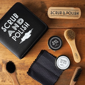 Könnte beinhalten: Ein Schuhpflege-Set mit einer schwarzen Ledertasche, zwei Schuhpolierdosen, einer Holzbürste, einem Tuch und einer Holzbürste mit dem Text "SCRUB & POLISH".