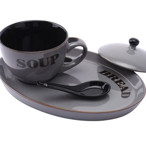 May include: Grey ceramic soup bowl with a black interior and the word "SOUP" printed on the side, a grey ceramic bread plate with the word "BREAD" printed on the side, a grey ceramic lid, and a black ceramic spoon.