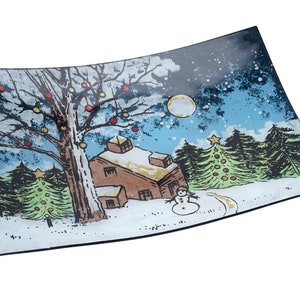 Puede incluir: Un plato para servir de vidrio con una escena de invierno pintada en él. La escena presenta una casa, un árbol con adornos rojos, un muñeco de nieve y un árbol de Navidad. El fondo es un cielo azul con estrellas y una luna llena.