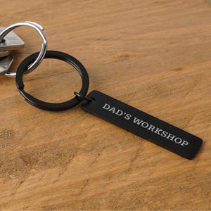 May include: Black metal keychain with a silver ring and a rectangular tag that says "DAD'S WORKSHOP".