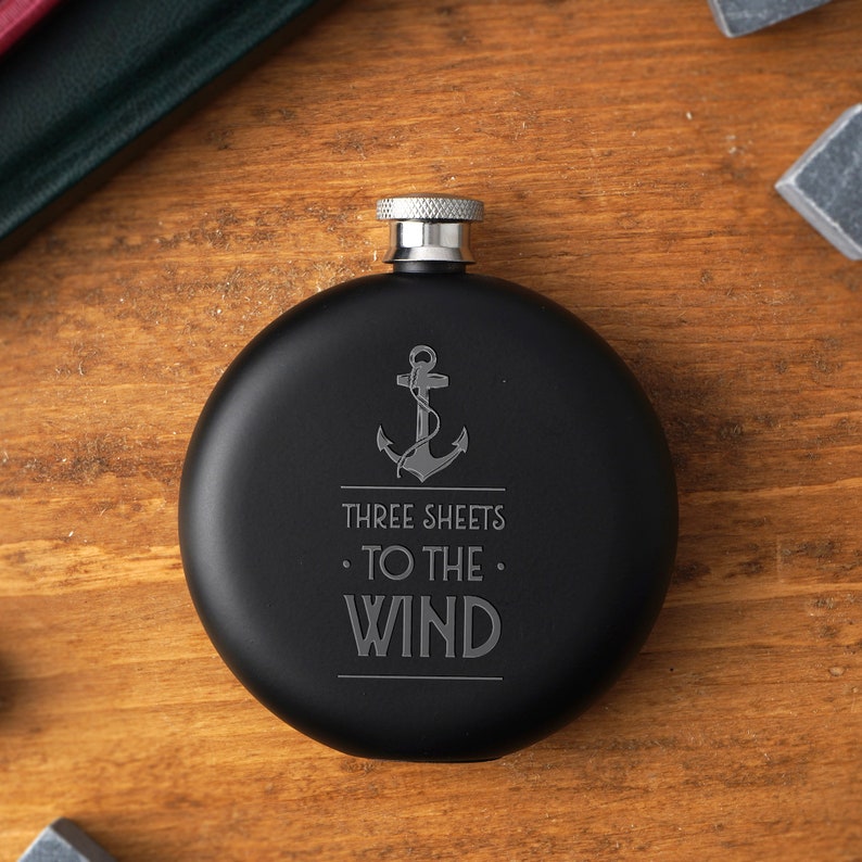 May include: Black metal flask with a silver lid and an engraved anchor with the text "Three Sheets To The Wind".