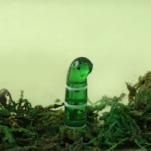 May include: A green glass worm with white stripes, standing upright in a bed of green moss.