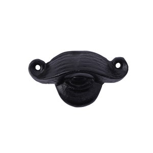 May include: Black cast iron bottle opener shaped like a mustache. The opener has a small hole on each side and a bottle opener on the bottom.