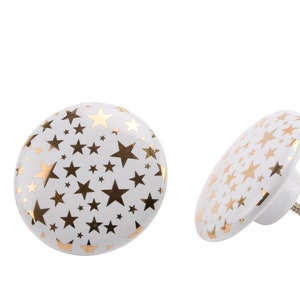 May include: Two white ceramic hooks with a gold star pattern. The hooks are designed to be mounted on a wall.