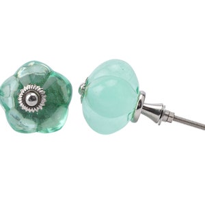 May include: Two green glass cabinet knobs with a silver metal base and screw. One knob is round and the other is shaped like a flower.