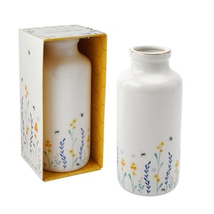 May include: Two white ceramic vases with a floral and bee design. The vases are in a box with a honeycomb pattern.