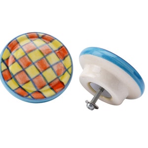 May include: Two ceramic cabinet knobs with a blue rim. One knob has a yellow and orange checkered pattern. The other knob is white with a blue rim.