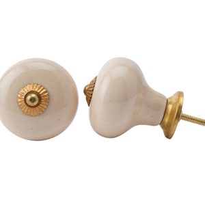 May include: Two ceramic knobs with a gold accent. One knob is round and the other is a rounded rectangle with a screw.