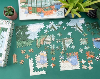 Op de afbeelding: Een 550-delige puzzel met een kleurrijke illustratie van een kas met planten, tuingereedschap en een kruiwagen. De puzzelstukjes zijn verspreid over een groene ondergrond.