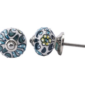 May include: Two ceramic cabinet knobs with a white base and a blue and green floral pattern. One knob is shown from the side, revealing a silver screw.