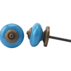 May include: Two turquoise blue ceramic cabinet knobs with a bronze-coloured metal base and decorative centre. One knob is shown from the front, the other from the side, revealing the screw for installation. Suitable for furniture or cabinetry.