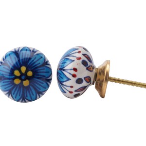 Pode incluir: Um botão de cerâmica azul e branco com um design floral. O botão tem um parafuso dourado e está preso a uma superfície branca.
