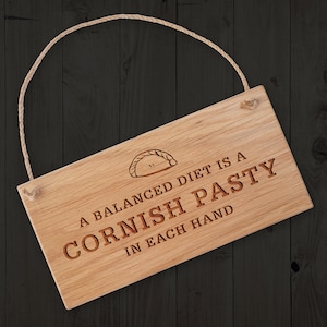 May include: A wooden sign with a rope hanger, featuring the text "A balanced diet is a Cornish pasty in each hand". The sign has a small illustration of a pasty.