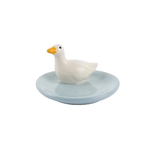 May include: A ceramic duck figurine with a yellow beak and black eyes sits on a light blue, round dish. The duck is white and the dish has a smooth surface. This decorative item is suitable for home decor.