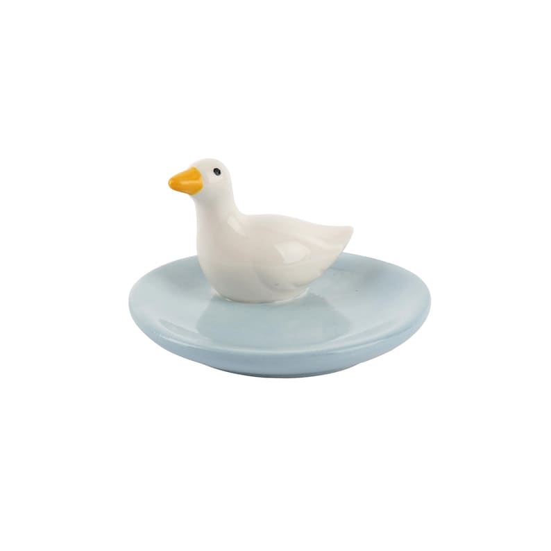 May include: A ceramic duck figurine with a yellow beak and black eyes sits on a light blue, round dish. The duck is white and the dish has a smooth surface. This decorative item is suitable for home decor.