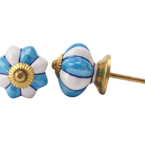 Op de afbeelding: Twee decoratieve keramische kastknoppen. De ene knop is bloemvormig met blauwe en witte bloemblaadjes en een gouden centrum. De andere knop is rond met blauwe en witte strepen en een gouden basis. Beide hebben messing schroeven.