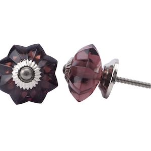 Könnte beinhalten: Zwei violette Glas-Schrankknöpfe, einer mit Sternform und der andere rund. Die Knöpfe haben eine silberne Metallbasis und eine Schraube.