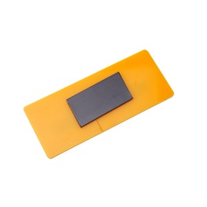 Op de afbeelding: Een kleine, rechthoekige, gele magneet met een zwarte rechthoekige magneet die in het midden is ingebed.