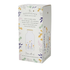 May include: White ceramic bottle vase with a floral design featuring bees and flowers. The vase is packaged in a box with a floral design and the text "The Beekeeper Ceramic Bottle Vase".
