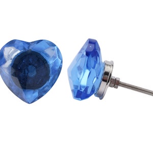 Peut inclure: Deux boutons de porte en verre bleu, l'un en forme de cœur et l'autre en forme de diamant, avec une vis argentée.