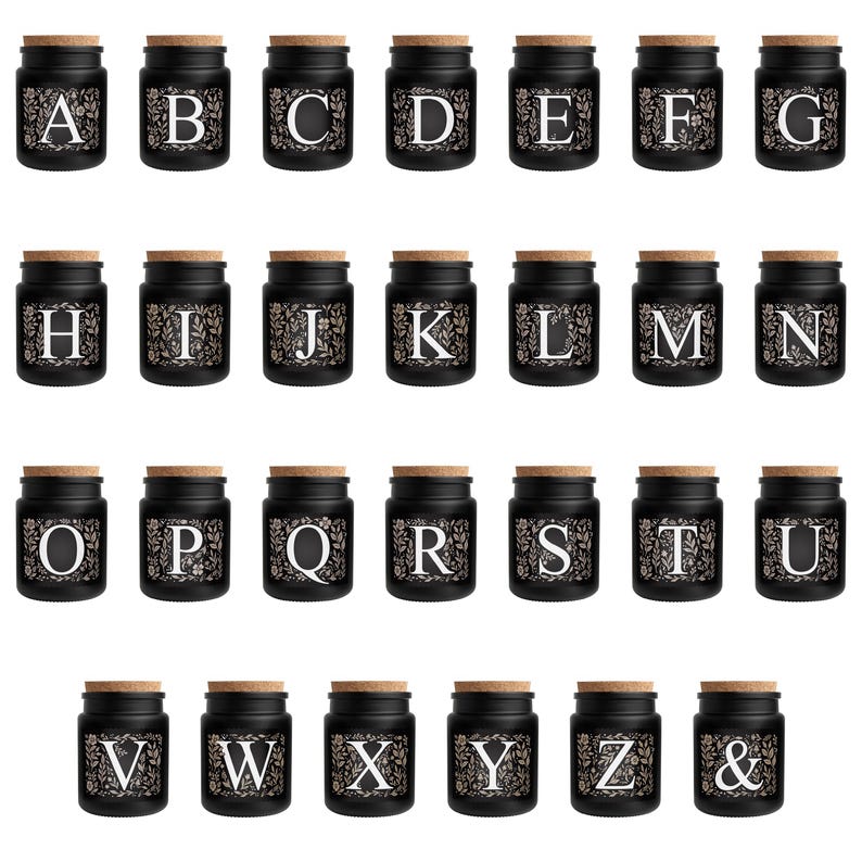 Puede incluir: Un conjunto de peque&ntilde;os frascos de vidrio negro con tapas de corcho, cada uno con una letra diferente del alfabeto en una fuente floral blanca. Los frascos est&aacute;n dispuestos en filas, ideales para regalos personalizados o almacenamiento.