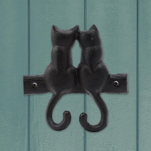 May include: Black cast iron wall hooks shaped like two cats sitting back to back with their tails curled into hooks.