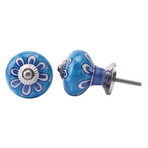 May include: Two blue ceramic cabinet knobs with a floral design. The knobs have a silver-coloured base and screw. The floral design is white and dark blue on a light blue background. The knobs are round and have a smooth, glossy finish.