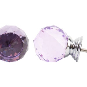 Puede incluir: Dos pomos de armario de cristal morado con base plateada y tornillo. Los pomos son facetados y tienen forma de diamante.