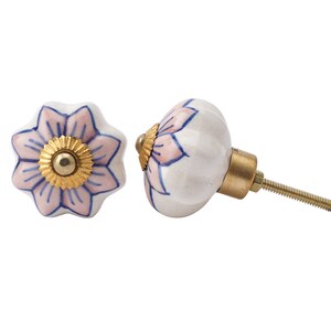 May include: Two ceramic cabinet knobs with a floral design. The knobs are white with pink and blue flower petals and a gold centre. The hardware is gold-toned metal.