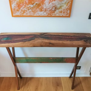 Peut inclure: Une console en bois avec un plateau en bois brut et une incrustation de résine colorée. La console a un piétement métallique en forme de croisillon.