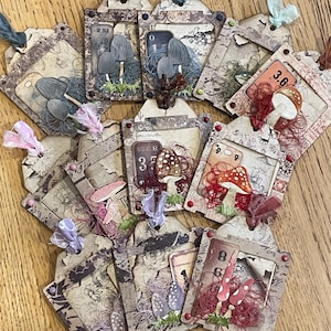 Peut inclure: Une collection d'étiquettes en papier faites à la main avec une esthétique vintage. Chaque étiquette présente des illustrations de champignons, des éléments décoratifs et de petits accents en tissu. Les étiquettes ont un aspect vieilli avec diverses couleurs, dont le marron, le gris, le rouge et le violet.