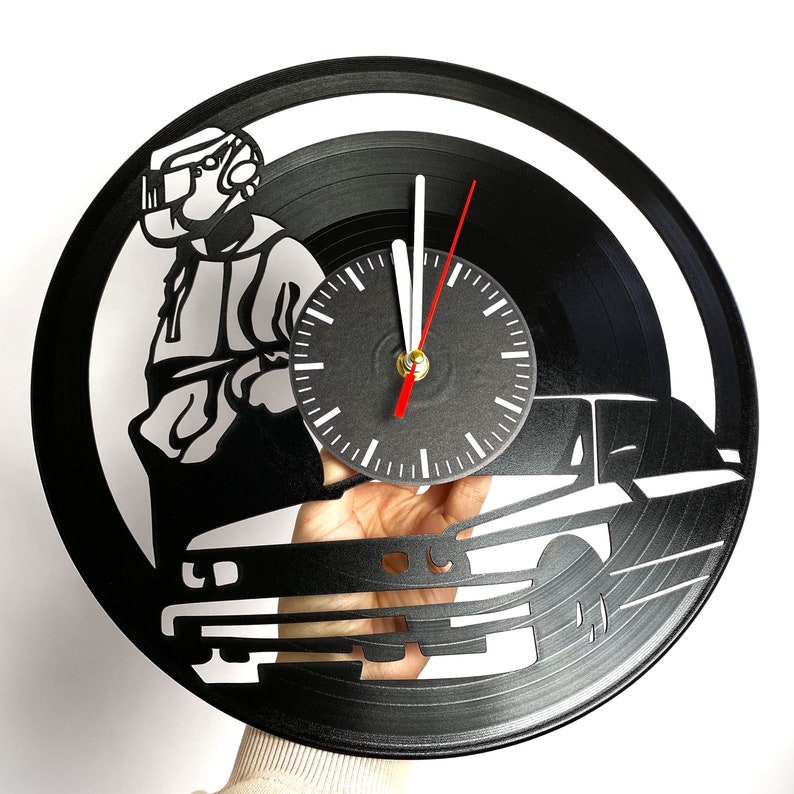 May include: Black vinyl record clock featuring a silhouette of a person wearing a helmet and a car. The clock face is white with black numbers and hands.
