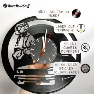 May include: A black vinyl record clock featuring a silhouette of a person driving a car. The clock is 12 inches in diameter and has a laser cut design. The clock face is a silkscreen sticker. The clock has a silent quartz movement.