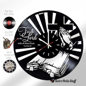 May include: Black vinyl record clock with a white and black design featuring a cross, praying hands, and an open book. The clock face is black with white numbers and hands. The text "Trust in the Lord with all thine heart Proverbs 3:5" is printed on the clock.