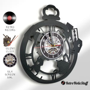 May include: Black wall clock shaped like a pocket watch with a silhouetted teapot and teacup design. The clock face is a smaller circle with a visible clock mechanism and Roman numeral markings.