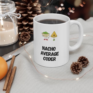 May include: White ceramic mug with a black and white graphic of a nacho chip and a bowl of salsa with the text "Nacho Average Coder".