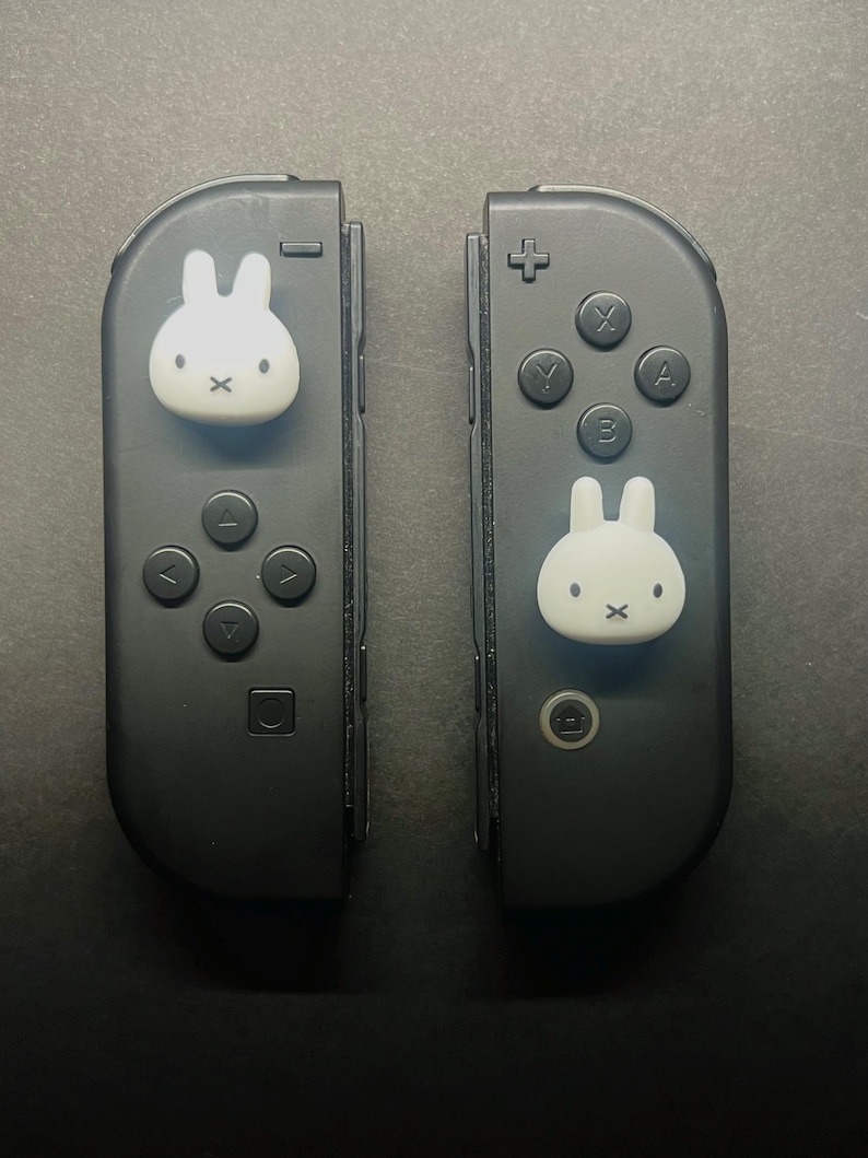 May include: Two black Nintendo Switch Joy-Con controllers. Each controller features a white bunny face on the joystick. The left controller has a directional pad and the right controller has the A, B, X, and Y buttons.