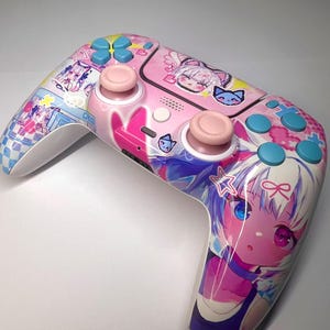 Può includere: Un controller di gioco rosa e bianco con grafica di personaggi in stile anime. Il controller presenta levette rosa, pulsanti blu e rosa e un design colorato con illustrazioni di cartoni animati. L'estetica generale è vibrante e giocosa.