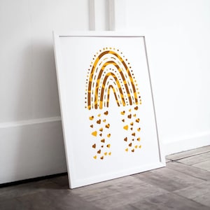 May include: White framed art print featuring a stylized rainbow design in shades of gold and brown. The rainbow is composed of curved lines and dotted patterns, with heart-shaped accents falling below. The artwork is leaning against a white wall.