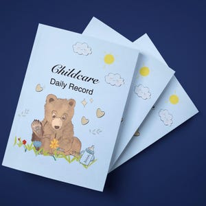 Può includere: Tre quaderni azzurri "Childcare Daily Record". Ogni copertina presenta un'illustrazione di orso marrone, nuvole, soli, cuori e un biberon. I quaderni sono impilati su una superficie blu scuro.