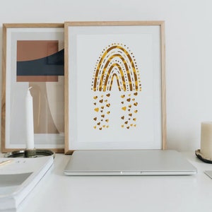 May include: A framed art print featuring a gold and brown rainbow design with heart-shaped accents. The artwork is displayed on a white desk alongside a laptop, candles, and other decorative items. The print is in a wooden frame.