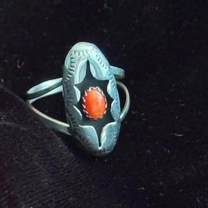 May include: A silver ring with an oval-shaped design. The ring features a star-shaped cutout with an orange stone in the center. The ring has a detailed, textured pattern around the edges.