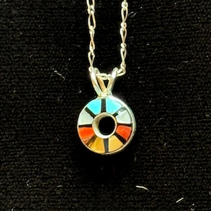 May include: A silver necklace with a circular pendant. The pendant features a colorful mosaic design with turquoise, red, yellow, and white segments. The necklace has a delicate chain and a small loop for the pendant.