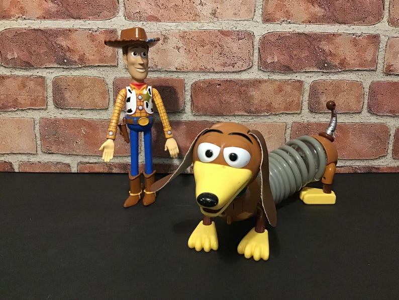 May include: Two Toy Story character figures: Sheriff Woody in a cowboy hat and Slinky Dog, a dachshund with a spring body. Woody wears a yellow shirt, vest, blue pants, and brown boots. Slinky Dog is brown, yellow, and gray.
