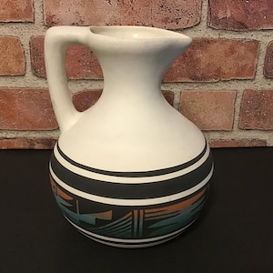 May include: White ceramic pitcher with a black and brown geometric design. The pitcher has a wide mouth and a handle.