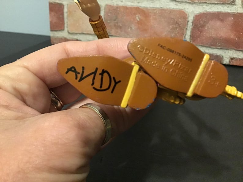 May include: Close-up of the bottom of a Woody action figure's boots. The word "ANDY" is written in black marker on the sole of one boot. The other boot has text that reads "Disney/Pixar Made in China".