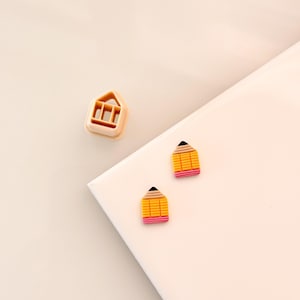 May include: Two yellow and pink pencil shaped earrings with black tips. The earrings are on a white surface.