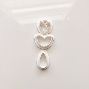 May include: Three white plastic cookie cutters shaped like a tulip, a leaf, and an oval.